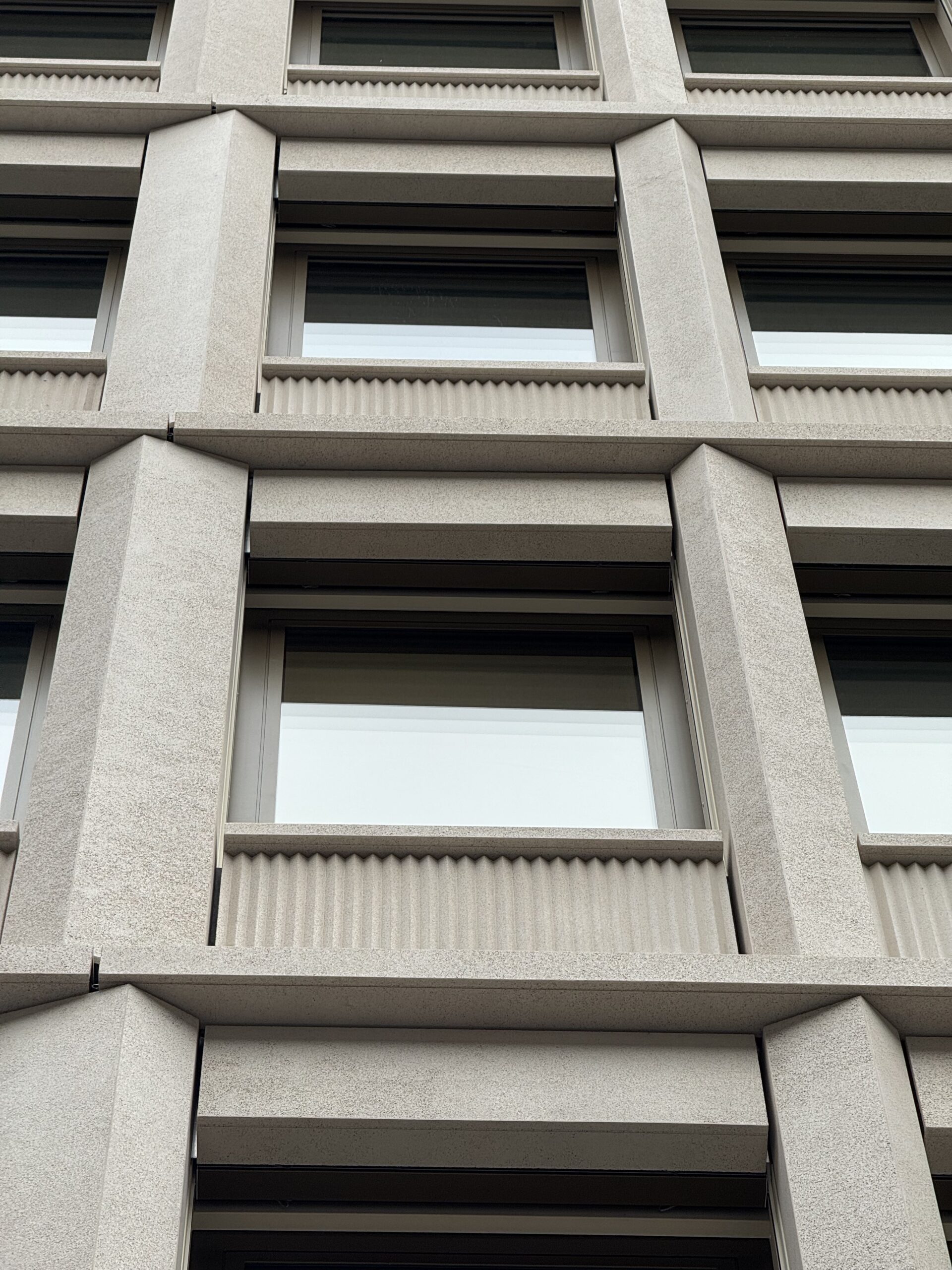 Détail de façade en dalles minérales Rebeton avec relief et trame régulière.