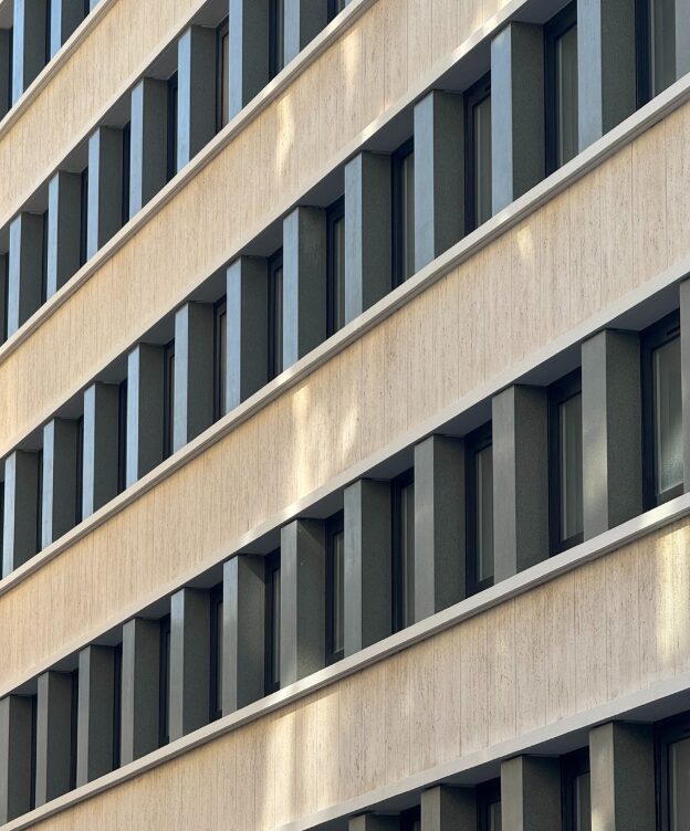 Façade contemporaine en bardage minéral avec alignement régulier de fenêtres verticales en retrait.